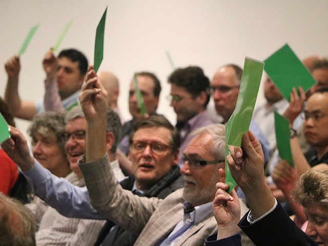 Deelnemers in de zaal houden stembriefjes omhoog tijdens de bijeenkomst van Afdeling Oost van de NBA over het visietraject