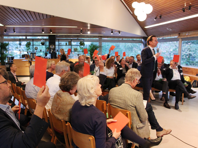 Deelnemers in de zaal houden rode stembriefjes omhoog