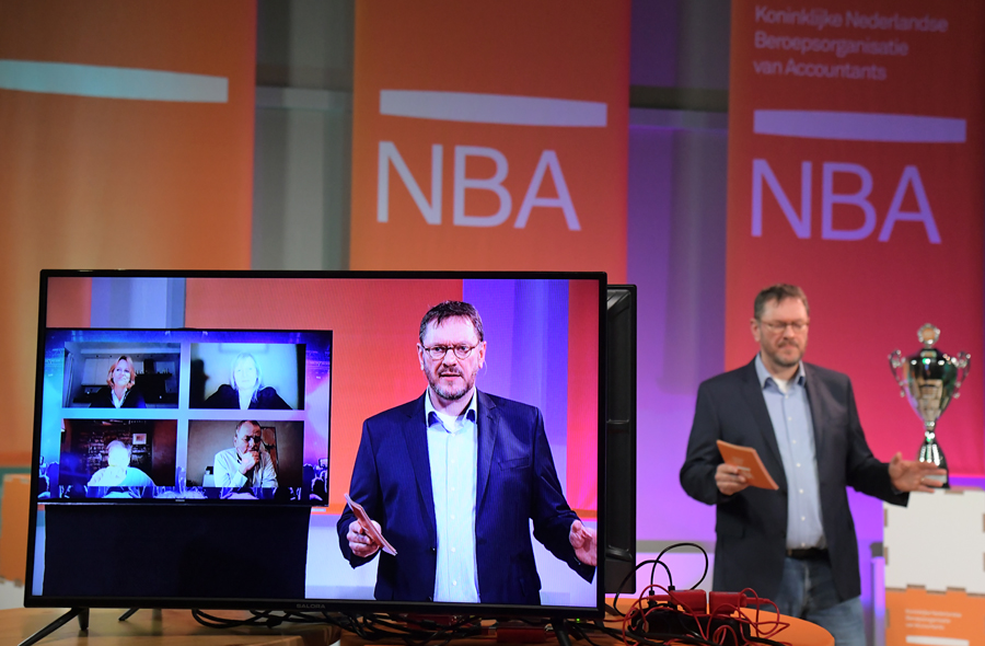 Lukas Burgering (NBA) op het podium en op een scherm met de juryleden