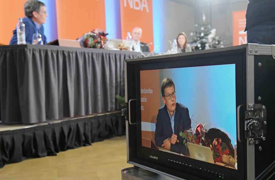 Frans van Schaik achter de bestuurstafel en op opnamescherm tijdens de NBA-ledenvergadering op 13 december 2021