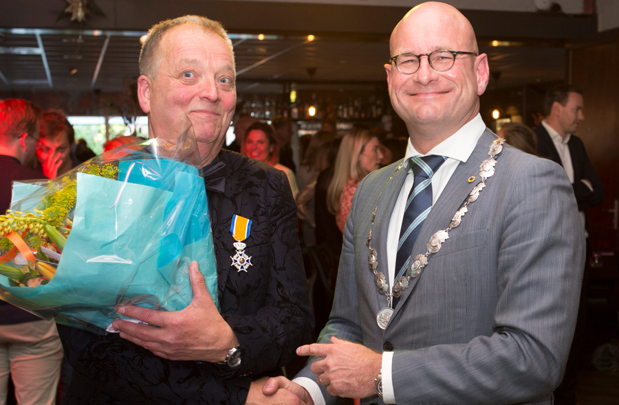 Hans Vonk met lintje en bloemen schudt de hand van de burgemeester