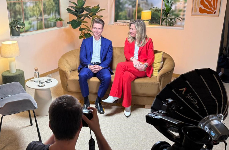 Bram Norder en Pauline de Wilde, zittend op een bank, worden gefotografeerd door cameraman